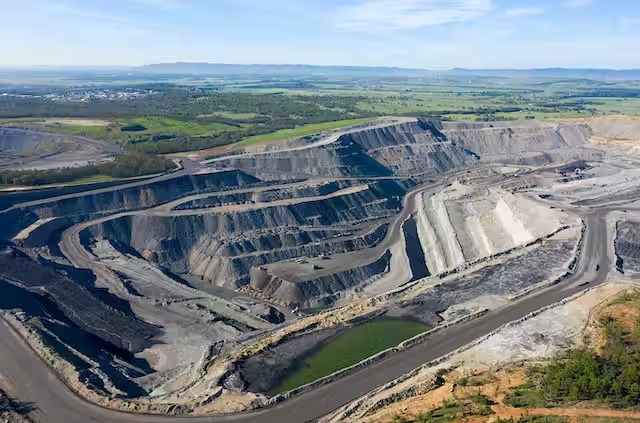 Bird's-eye view of an open pit mine, revealing extensive digging and heavy machinery at work.